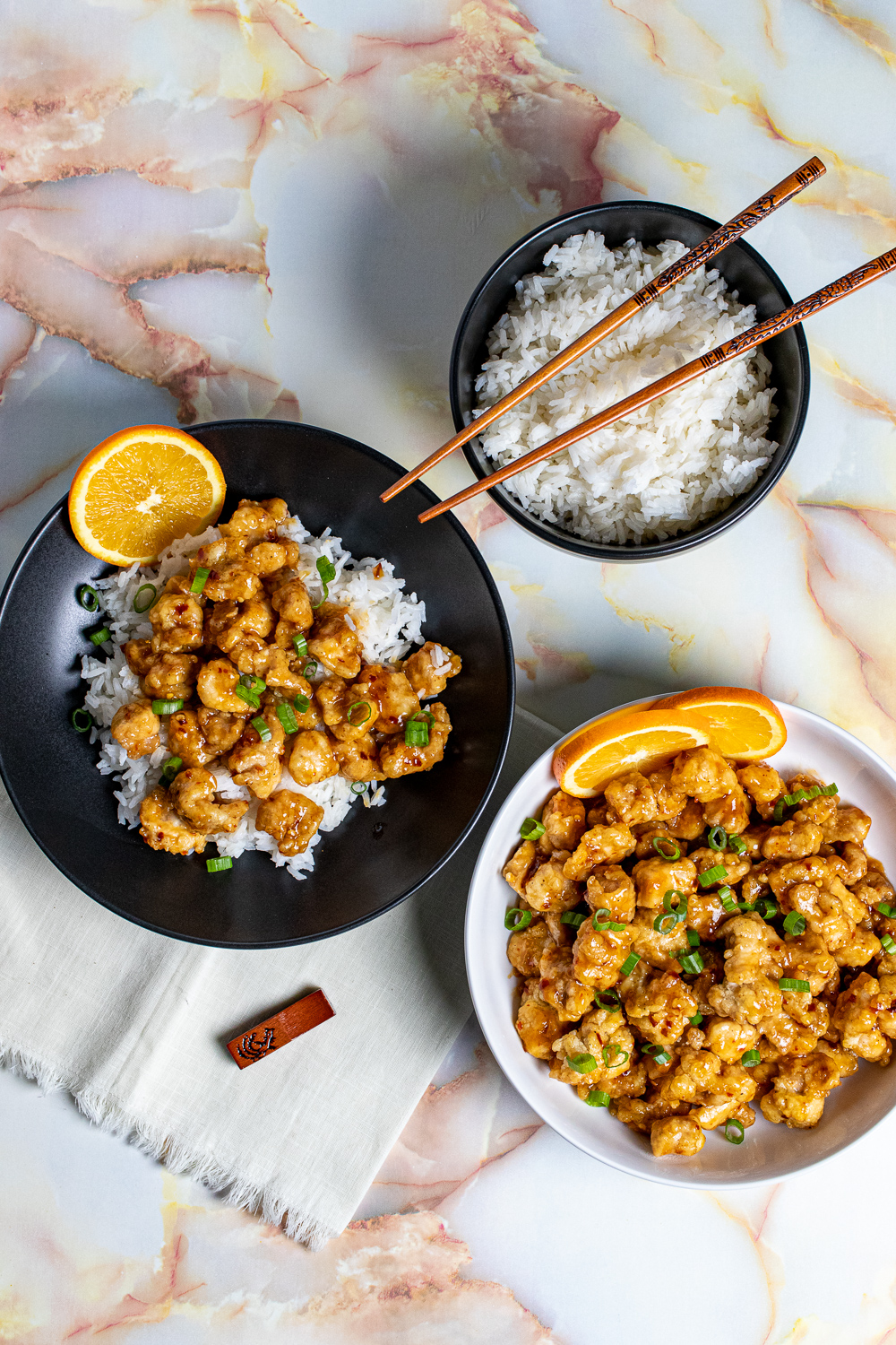 overhead view of orange chicken in bowls with rice and chopsticks