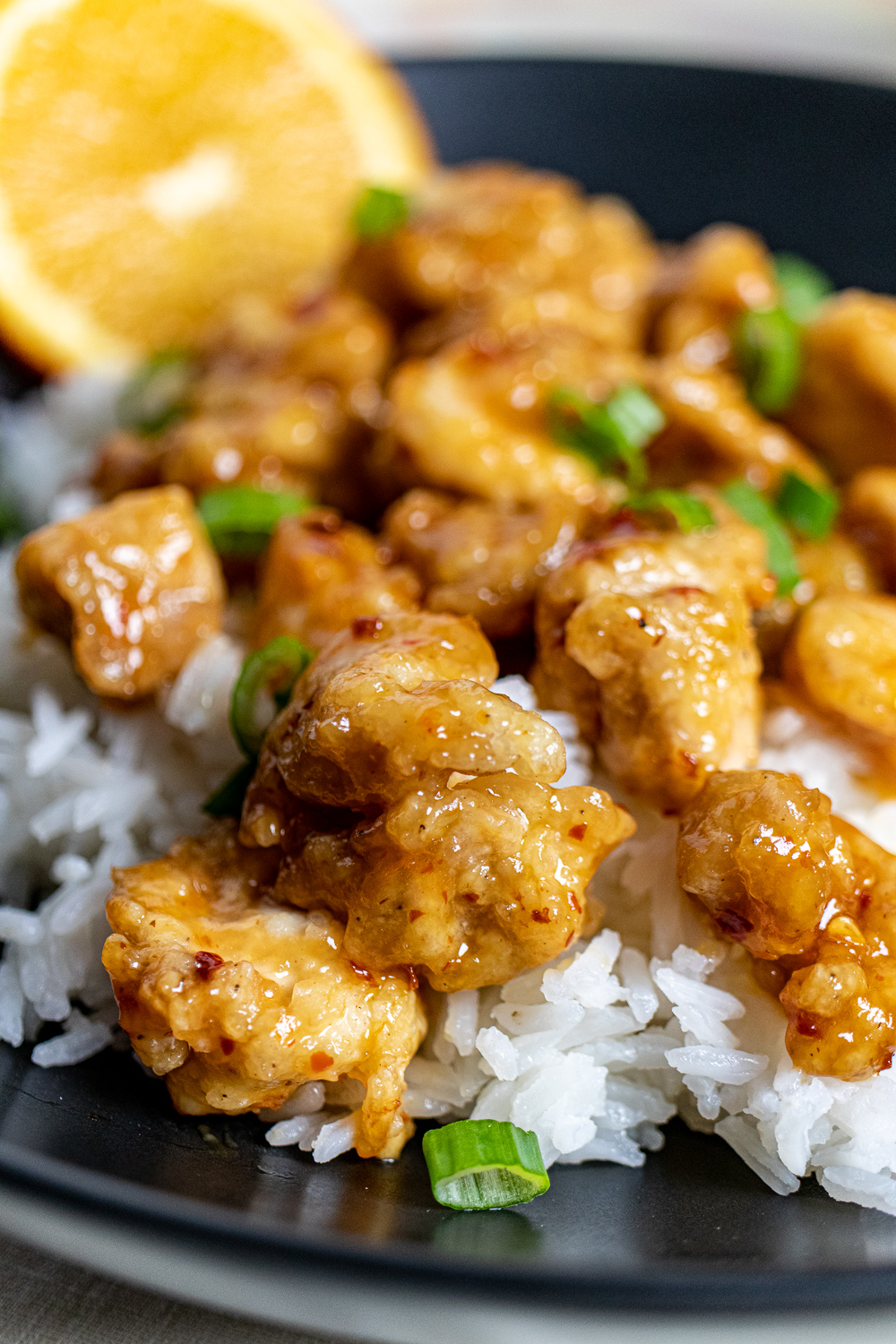 close up of orange chicken over rice in a black bowl
