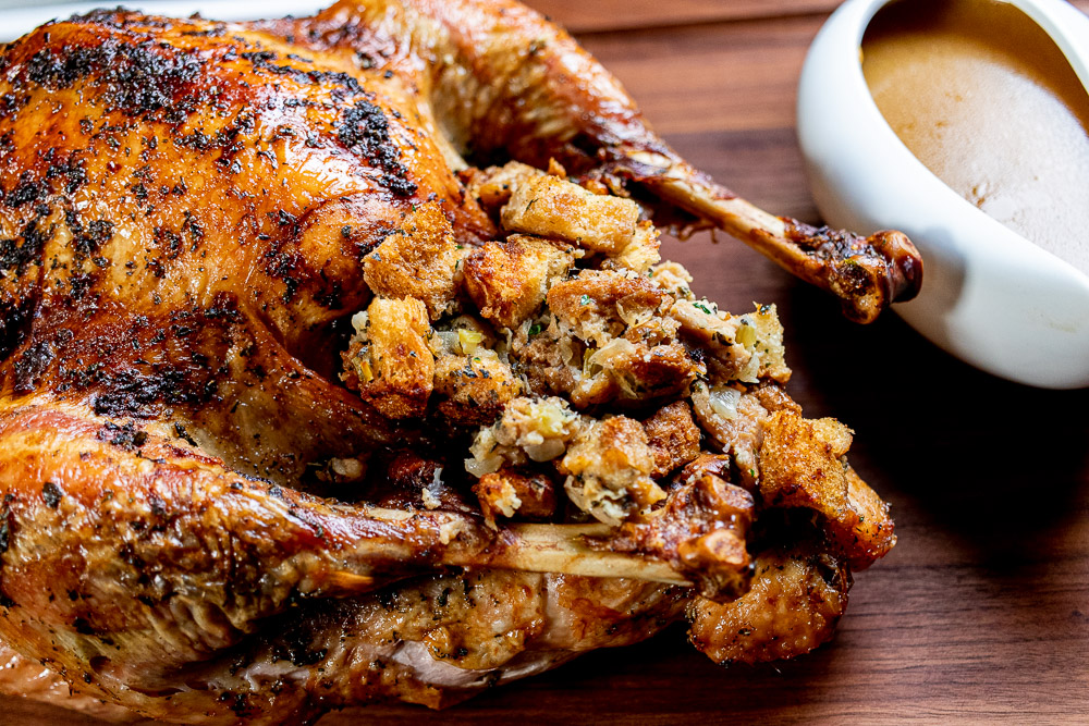 whole herb roasted turkey with stuffing and side of gravy on a wooden cutting board