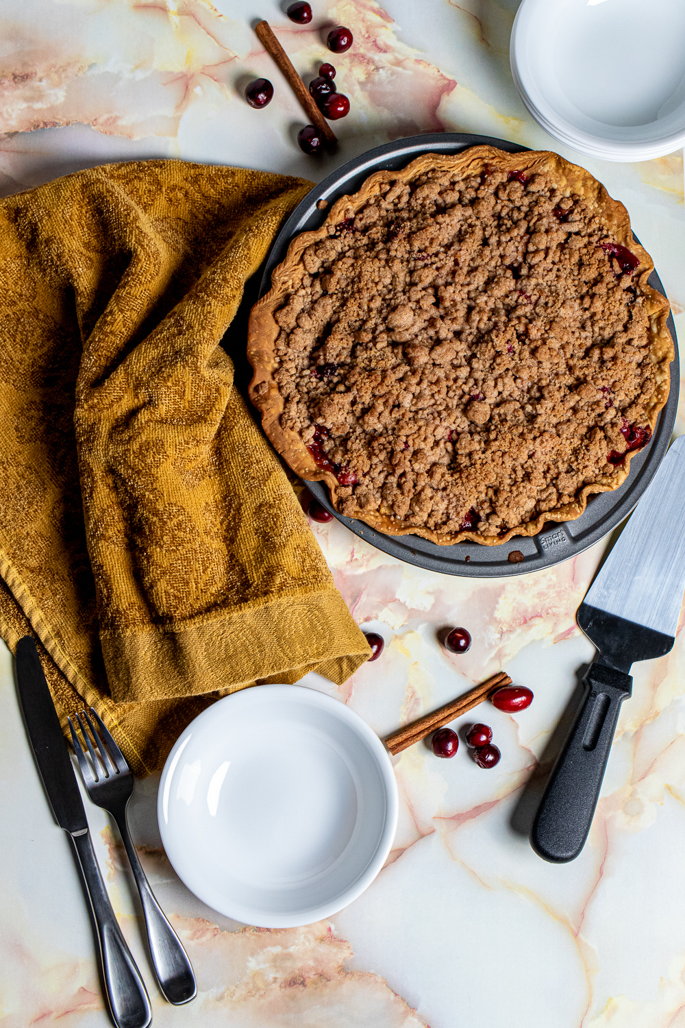 cranberry pear crumble pie with a yellow towel and pie cutter