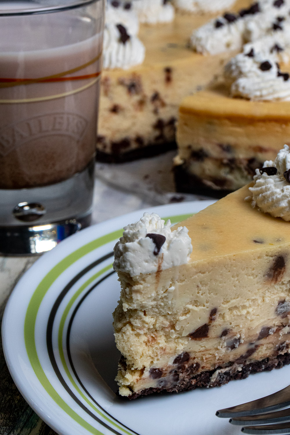 A slice of Bailey's cheesecake with chocolate chips and glass of Bailey's next to it.