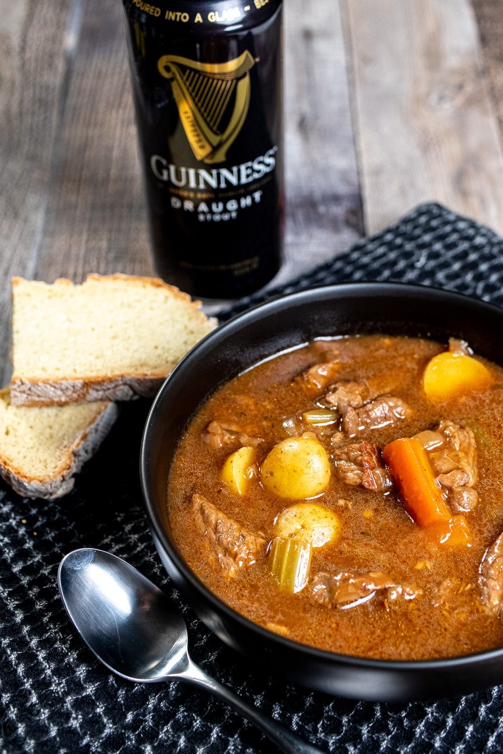 A black bowl of Guinness Irish stew served with Irish soda bread and a can of Guinness Draught behind it.