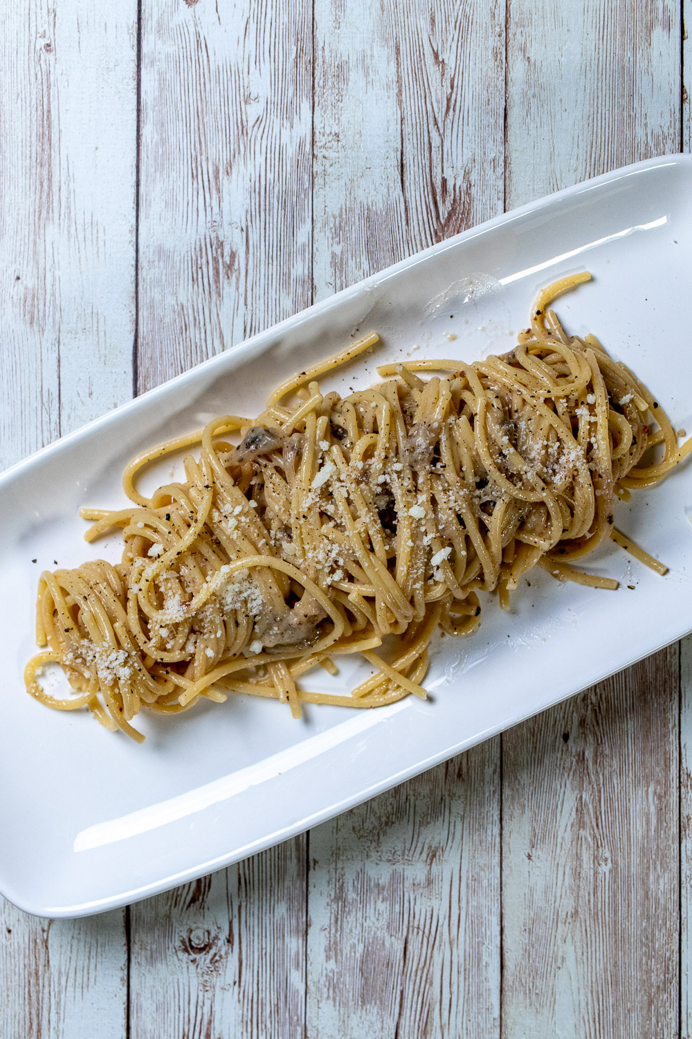 Cacio e pepe pasta made with thick spaghetti on a rectangular white plate.