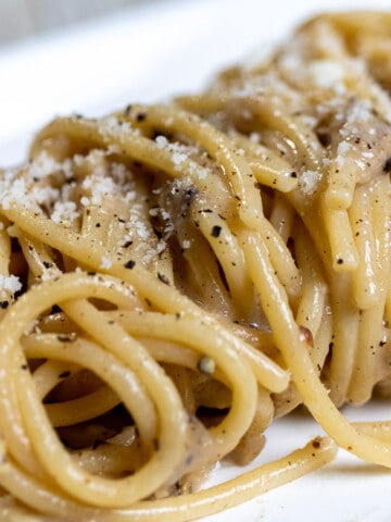 Cacio e pepe pasta made with thick spaghetti on a rectangular white plate.