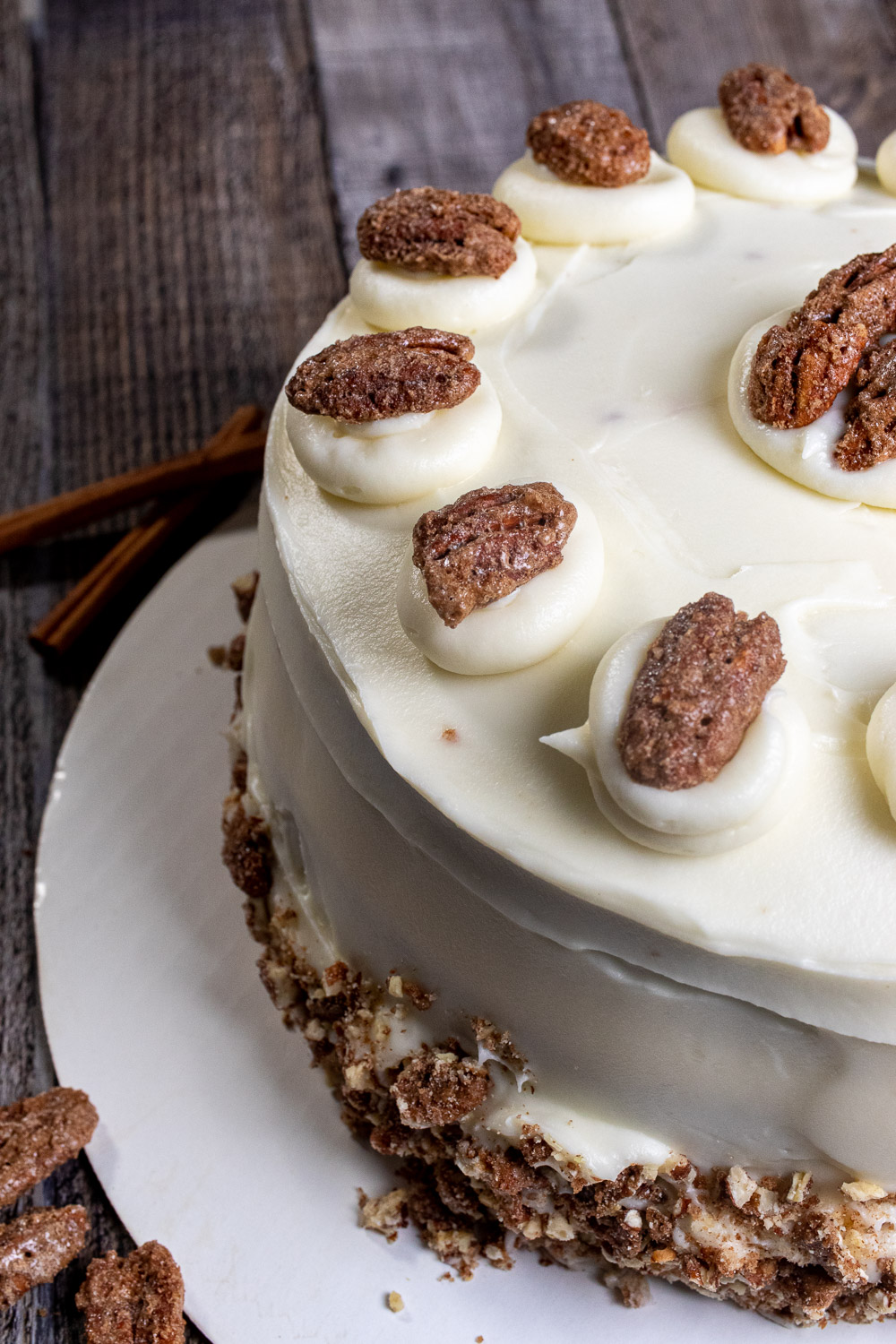 Angled view of a cream cheese frosted, 3-layer carrot cake with, decorated with candied pecans.