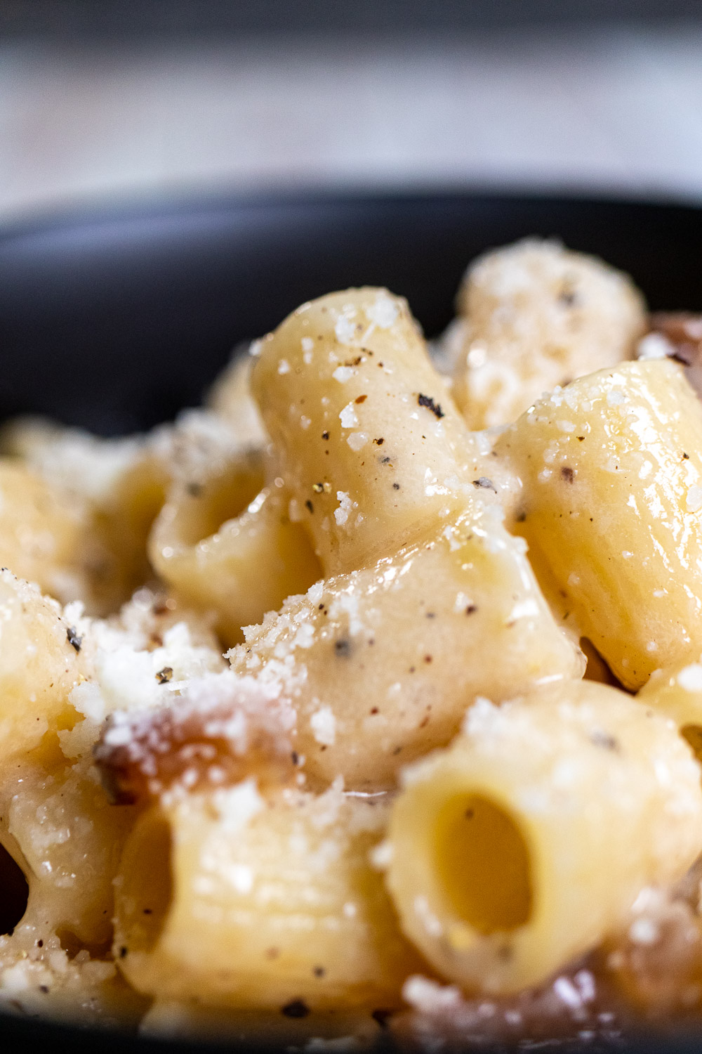 Close up of a black bowl filled with pasta alla gricia, made with short rigatoni noodles.