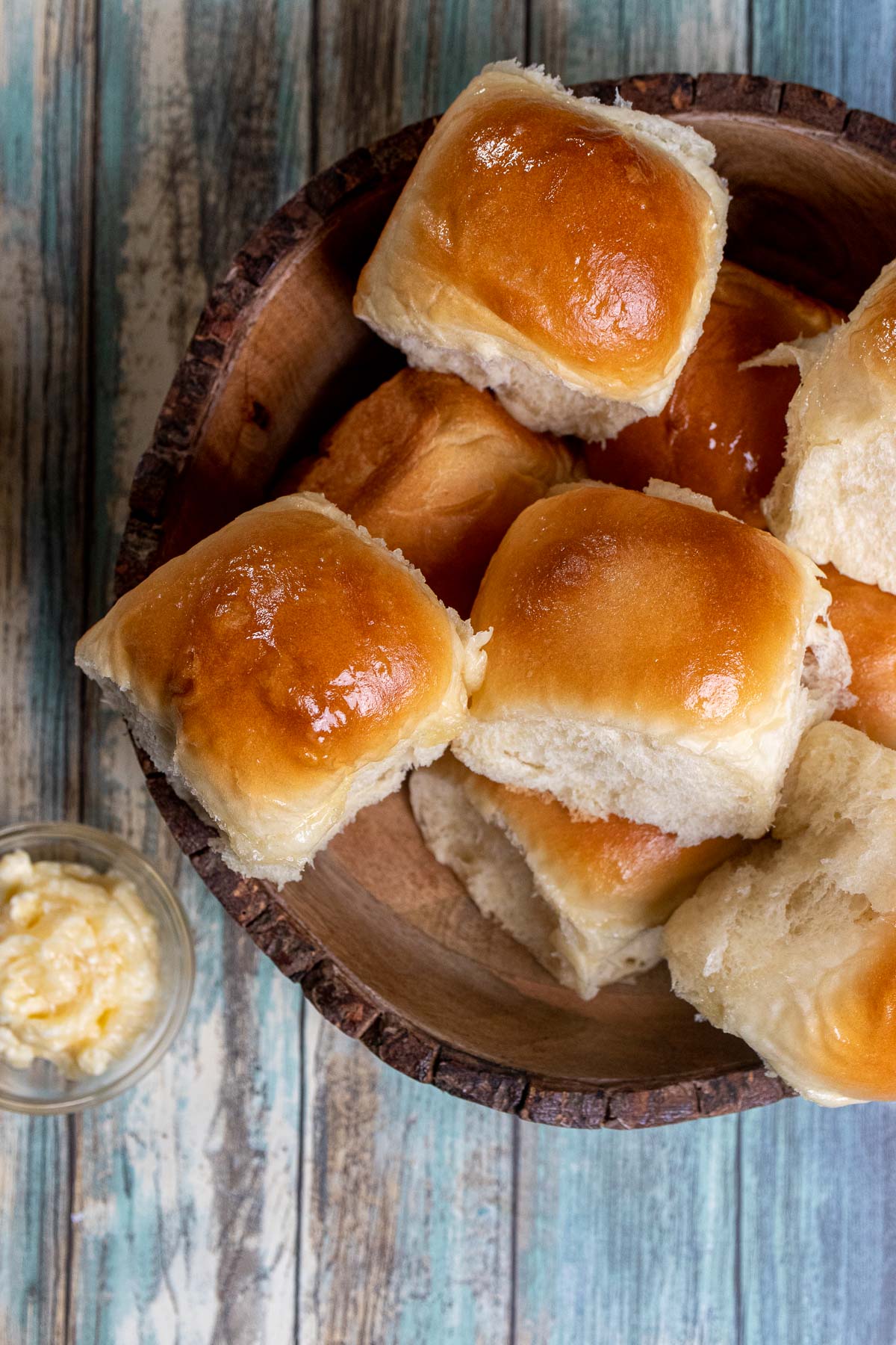 Overhead view of honey butter dinner rolls in a wooden bowl with a side of honey butter in a small dish.