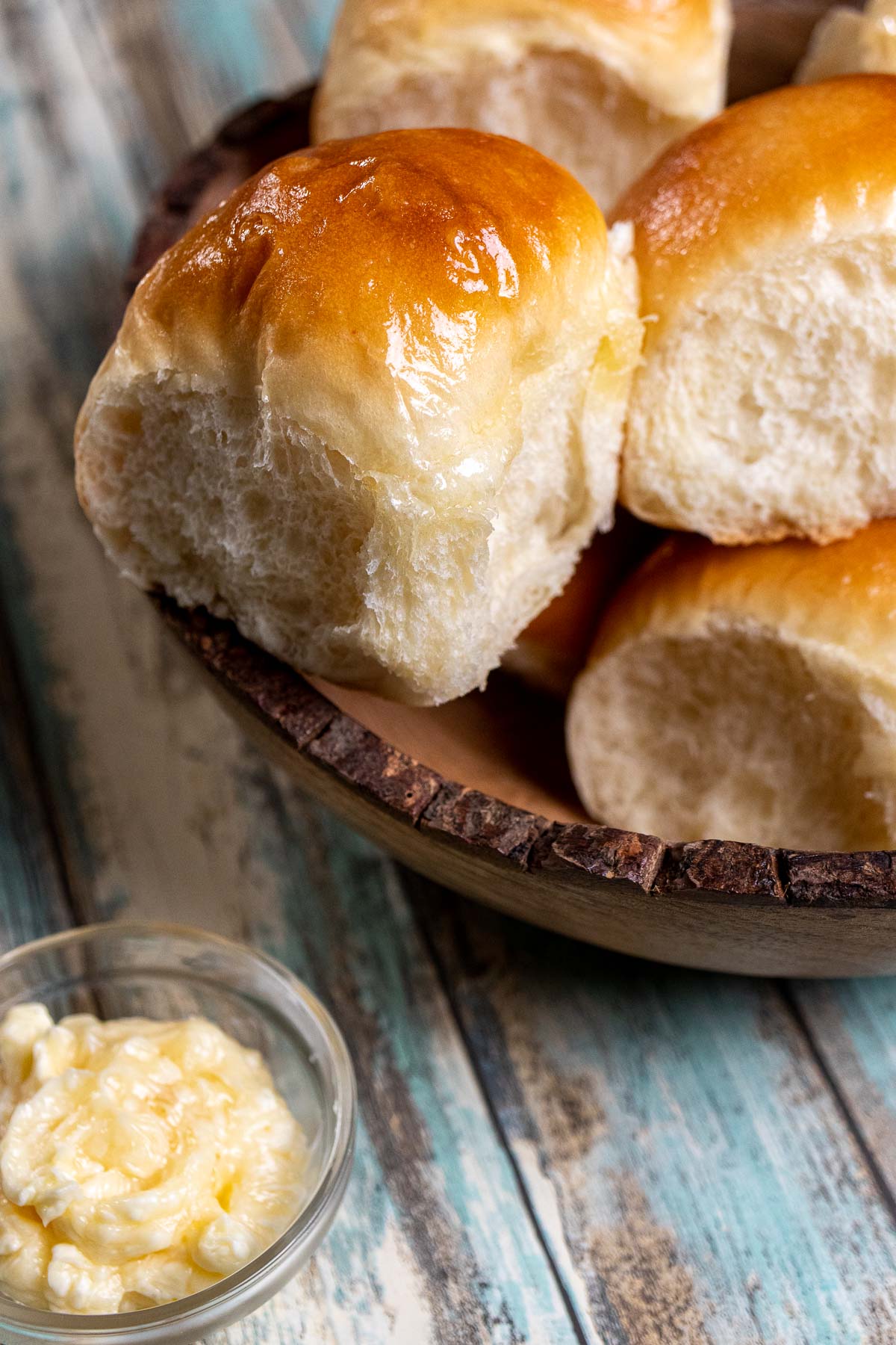 Honey butter dinner rolls in a wooden bowl with a side of honey butter in a small dish.