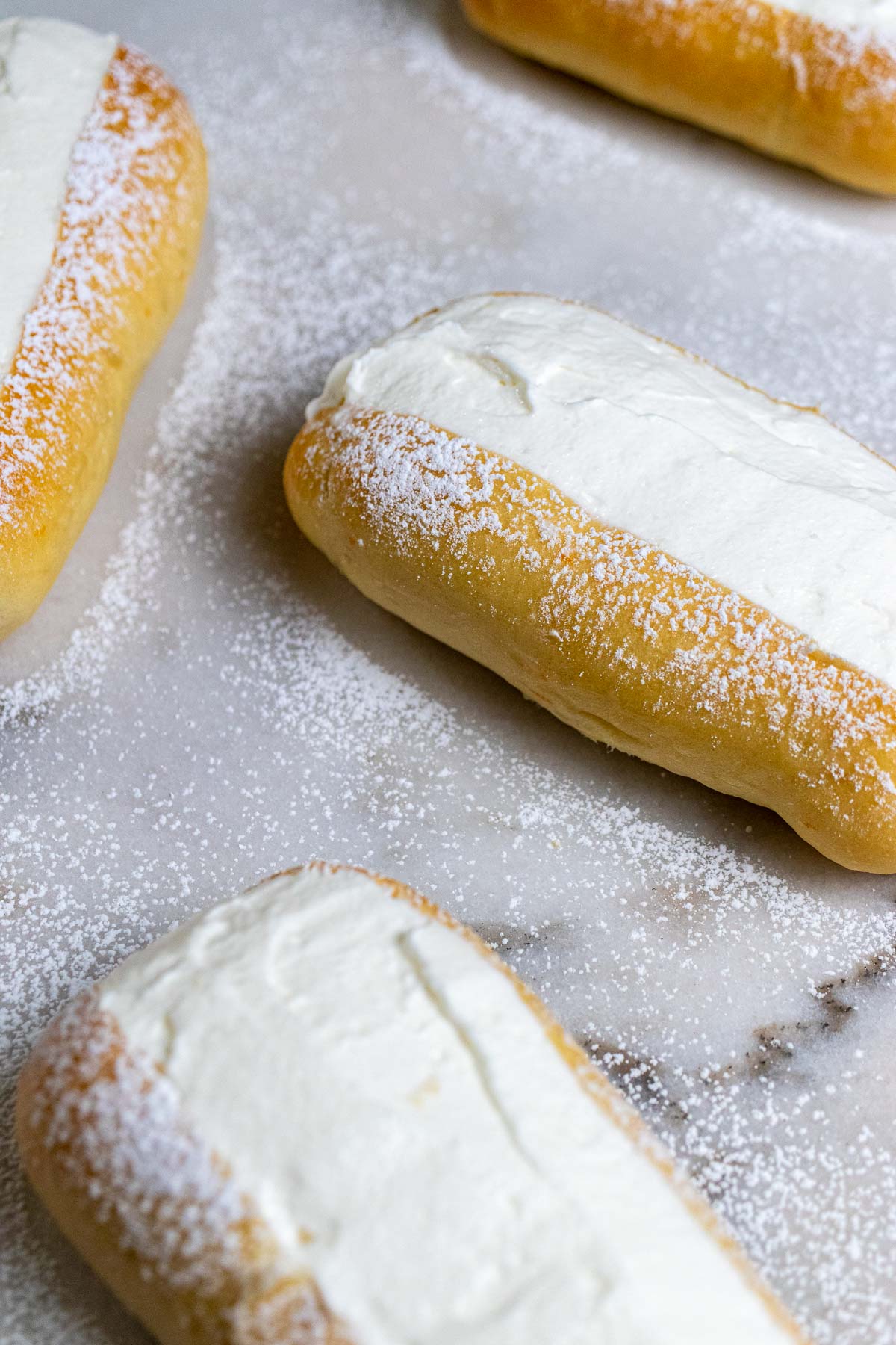 Roman maritozzi buns filled with whipped cream and dusted with powdered sugar on a marble counter.