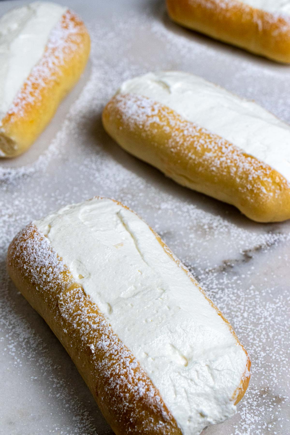 Roman maritozzi buns filled with whipped cream and dusted with powdered sugar on a marble counter.