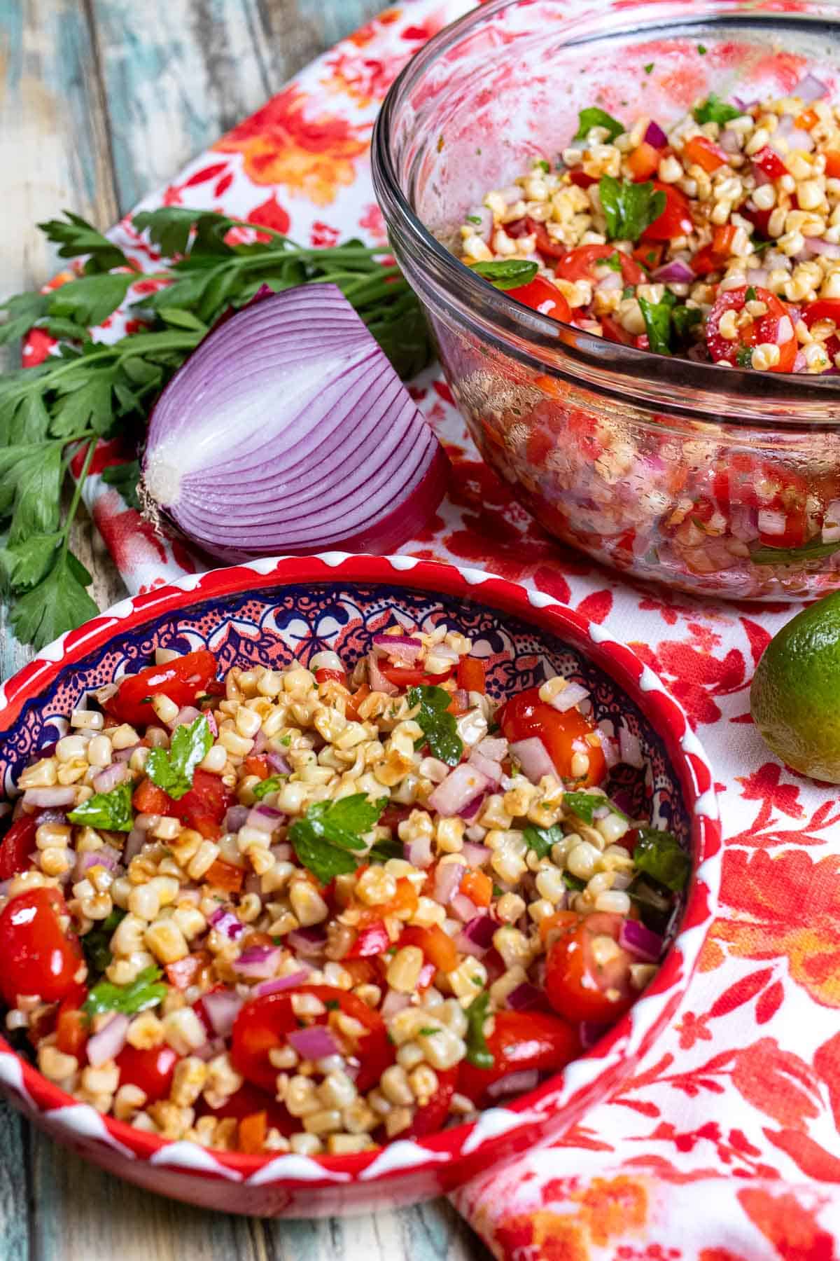 Roasted corn salad in a glass mixing bowl with a portion in front in a red and white bowl.