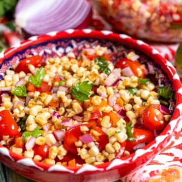 Close up view of a roasted corn salad in a red and white bowl on top of a red and white cloth.