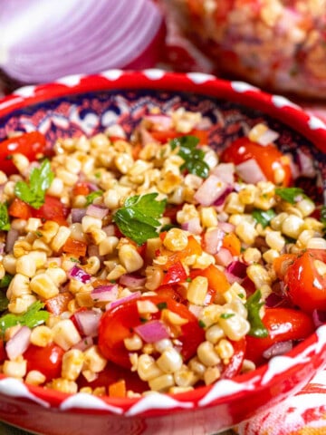 Close up view of a roasted corn salad in a red and white bowl on top of a red and white cloth.