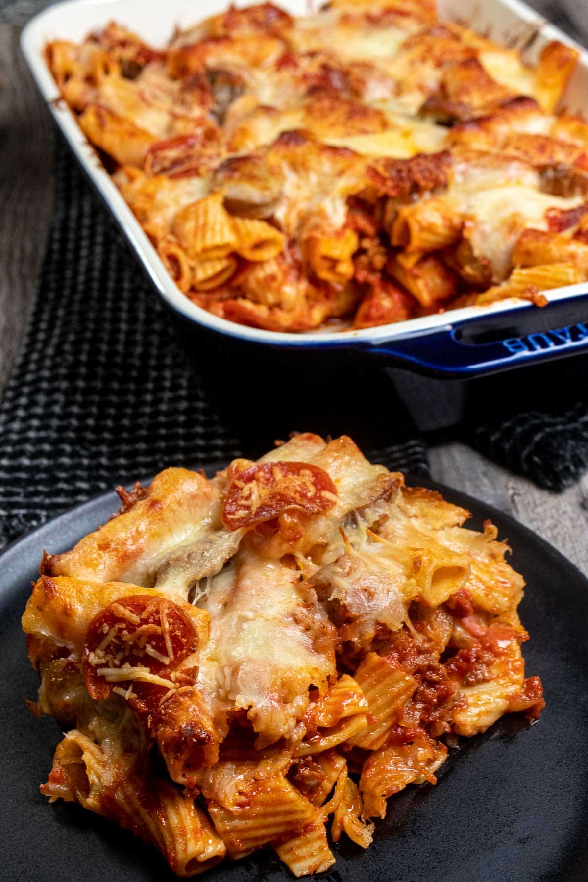 Large portion of baked rigatoni filled with sausage and meatballs on a black plate, with the rest of the baked pasta behind it.