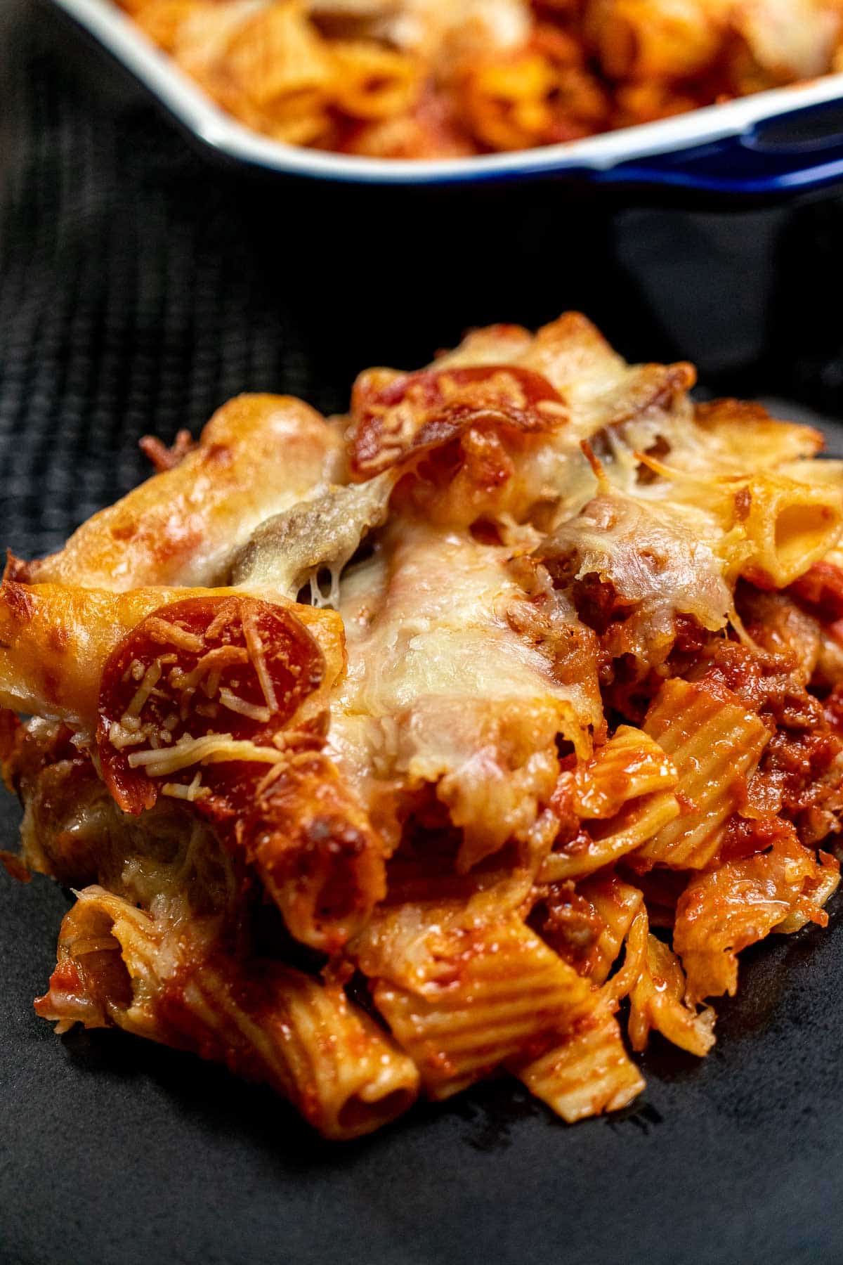 Large portion of baked rigatoni filled with sausage and meatballs on a black plate.
