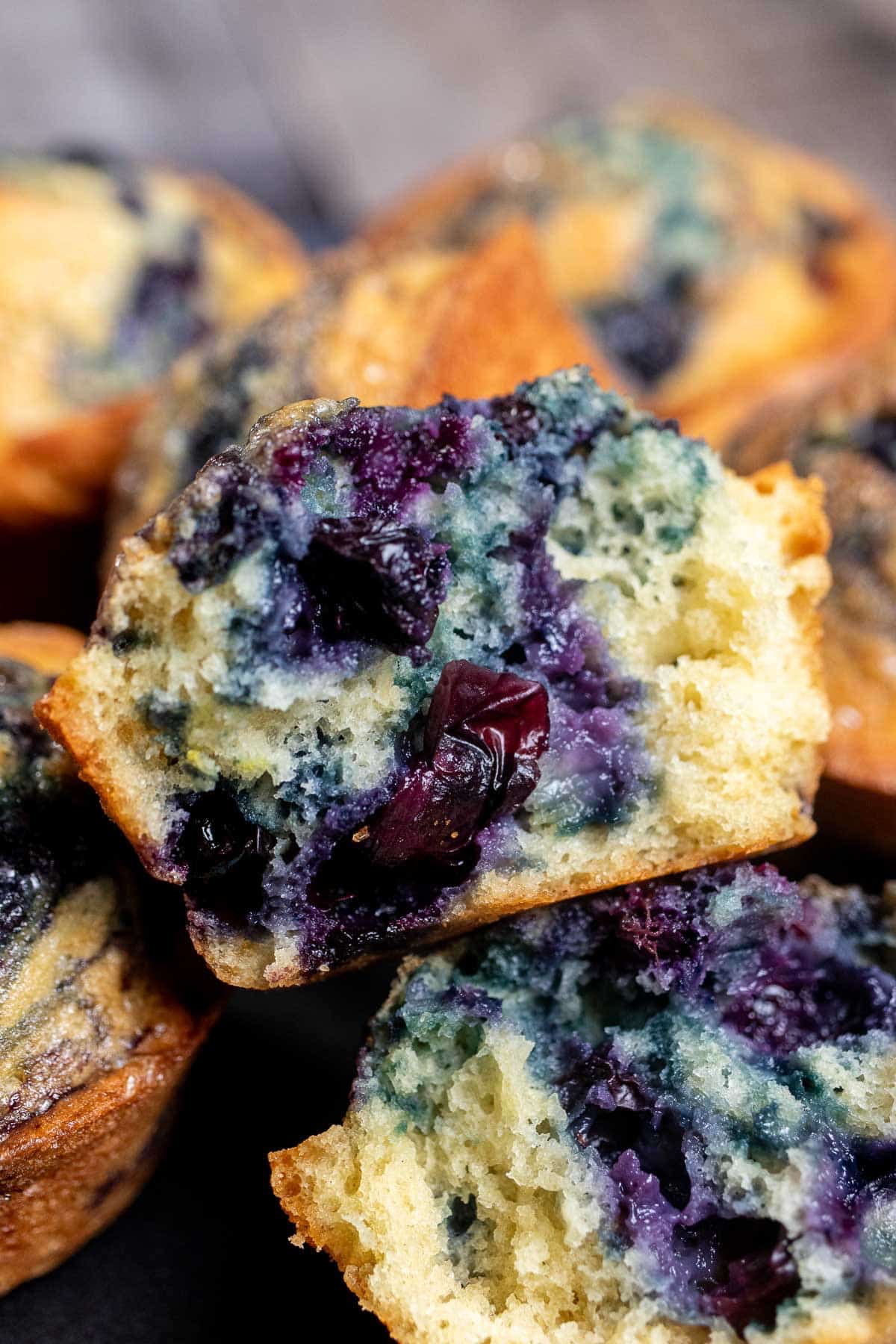 Close up view of a pile of blueberry swirl muffins centered on one cut open to show the blueberry swirls. 