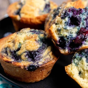 Close up view of bakery style blueberry swirl muffins and an open muffin on a black plate.