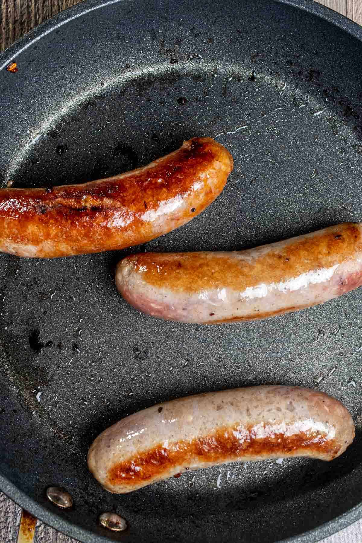 Searing and browning Italian sausages in a skillet.
