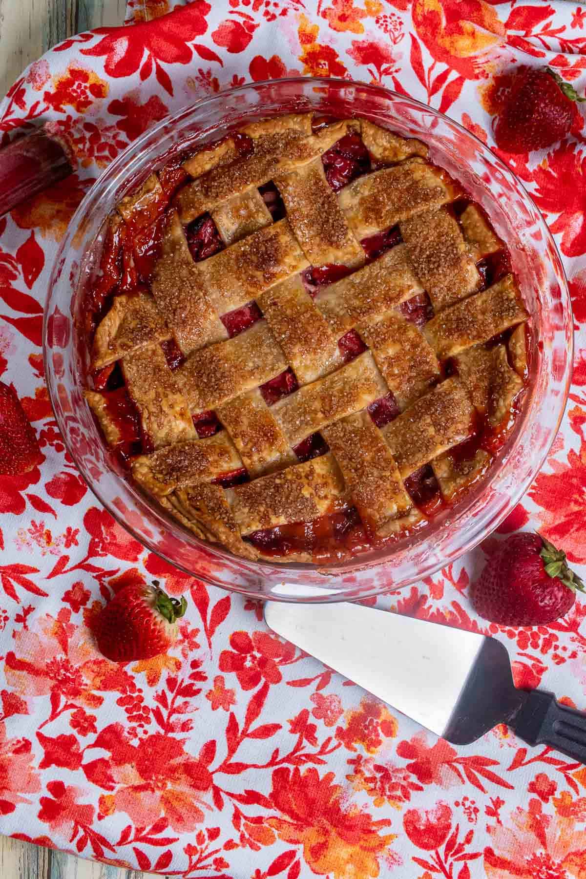Overhead view of strawberry rhubarb lattice pie on a red and white floral cloth.
