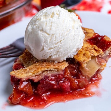 A slice of strawberry rhubarb lattice pie on a white plate, topped with vanilla ice cream.