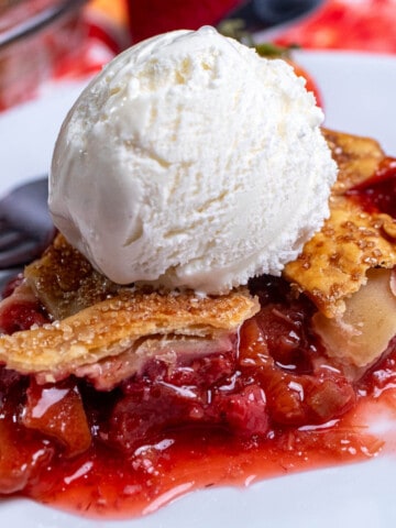 A slice of strawberry rhubarb lattice pie on a white plate, topped with vanilla ice cream.