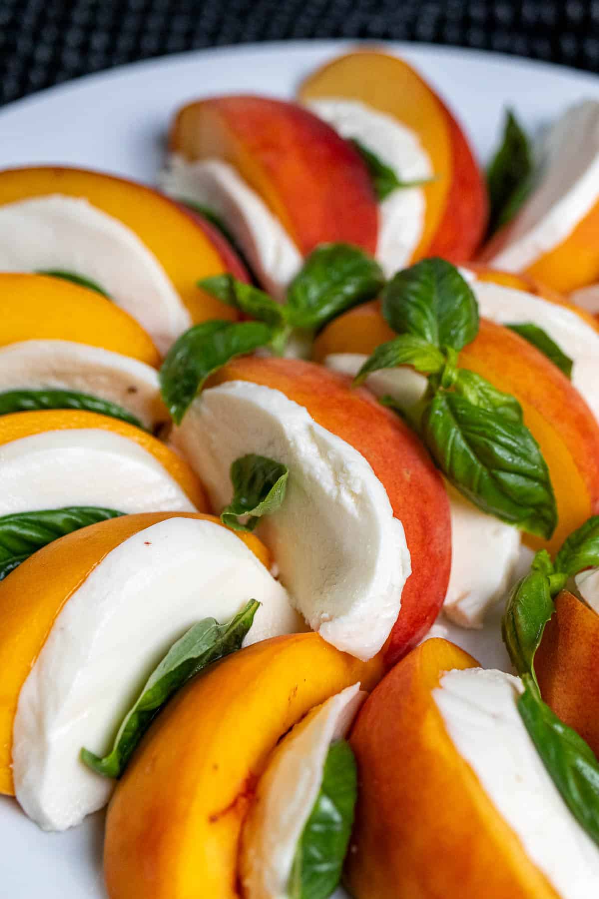 Sliced of peaches and mozzarella with basil arranged on a large white plate before being topped with dressing.