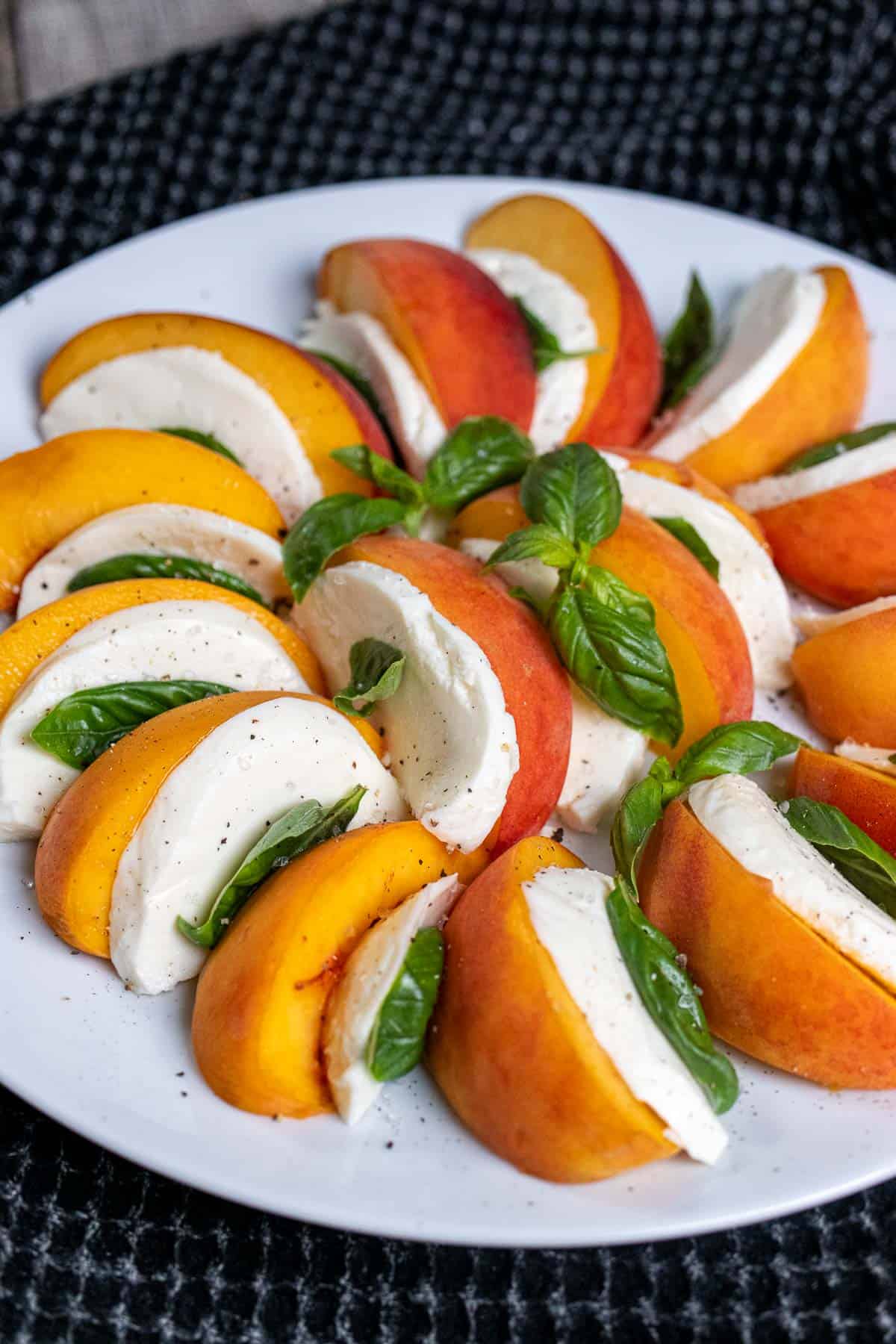 Angled view of a peach caprese salad on a white plate, without a dressing