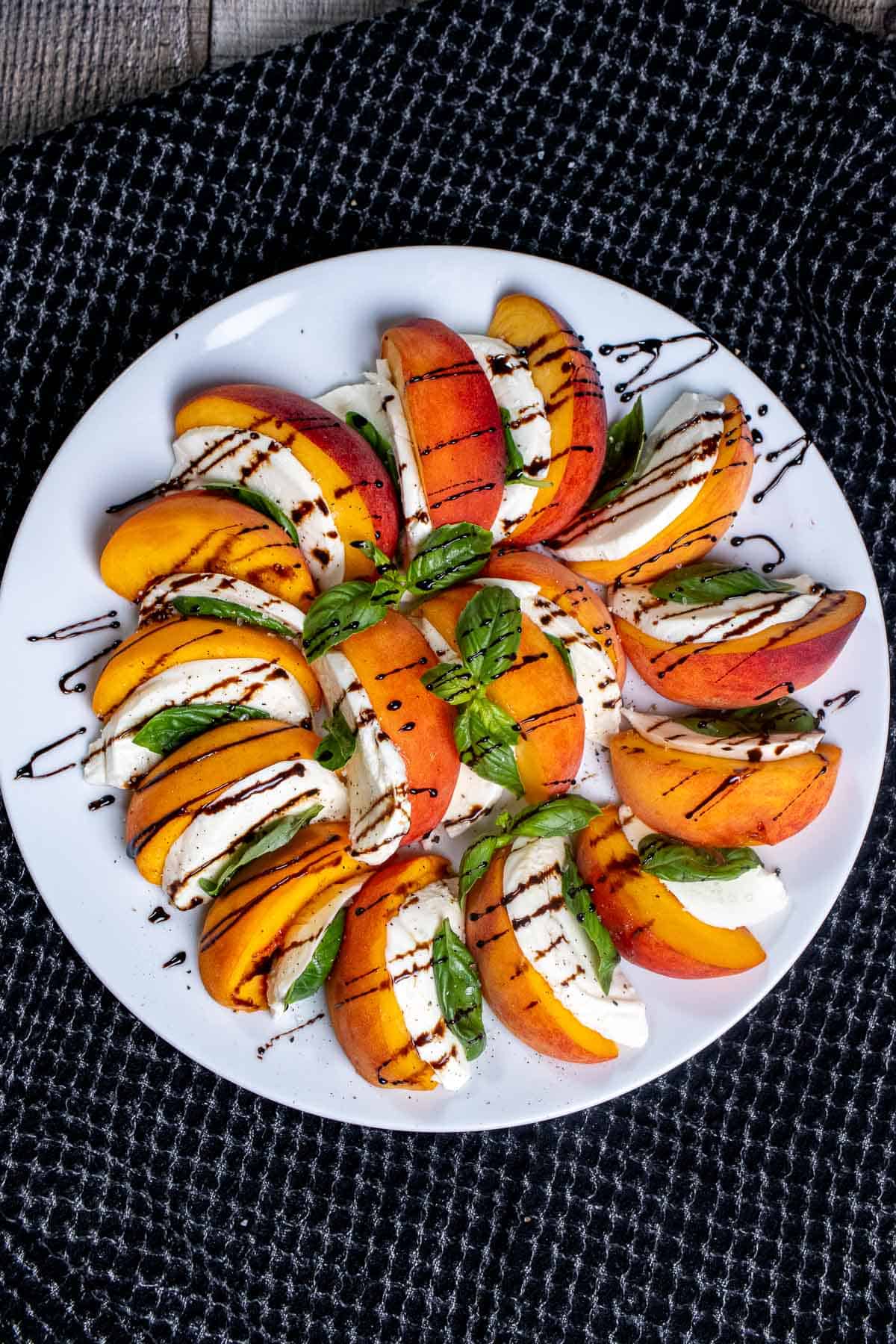 Overhead view of a peach caprese salad, on a white plate with a drizzle of balsamic glaze over top.