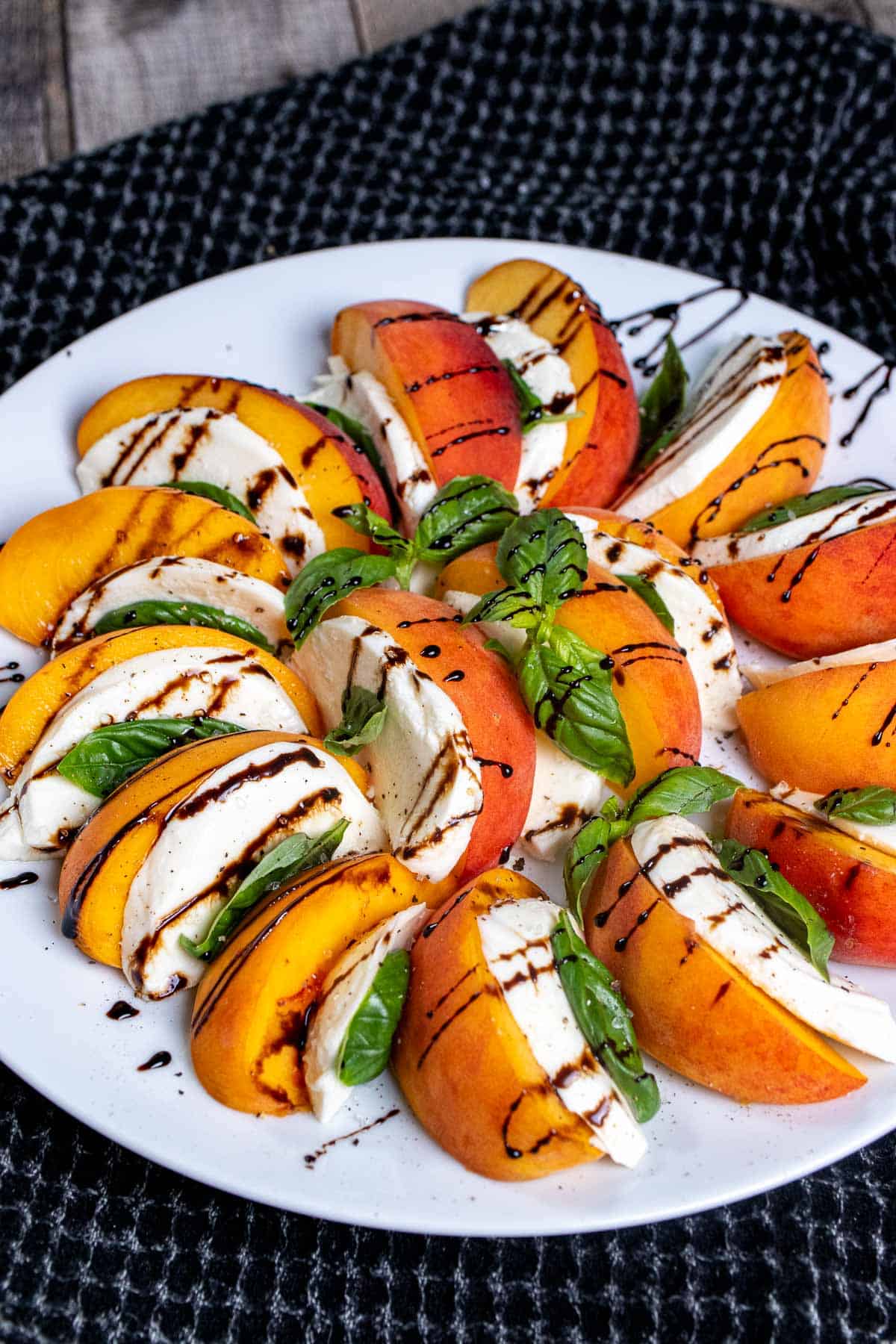 Angled view of a peach caprese salad, on a white plate with a drizzle of balsamic glaze over top.