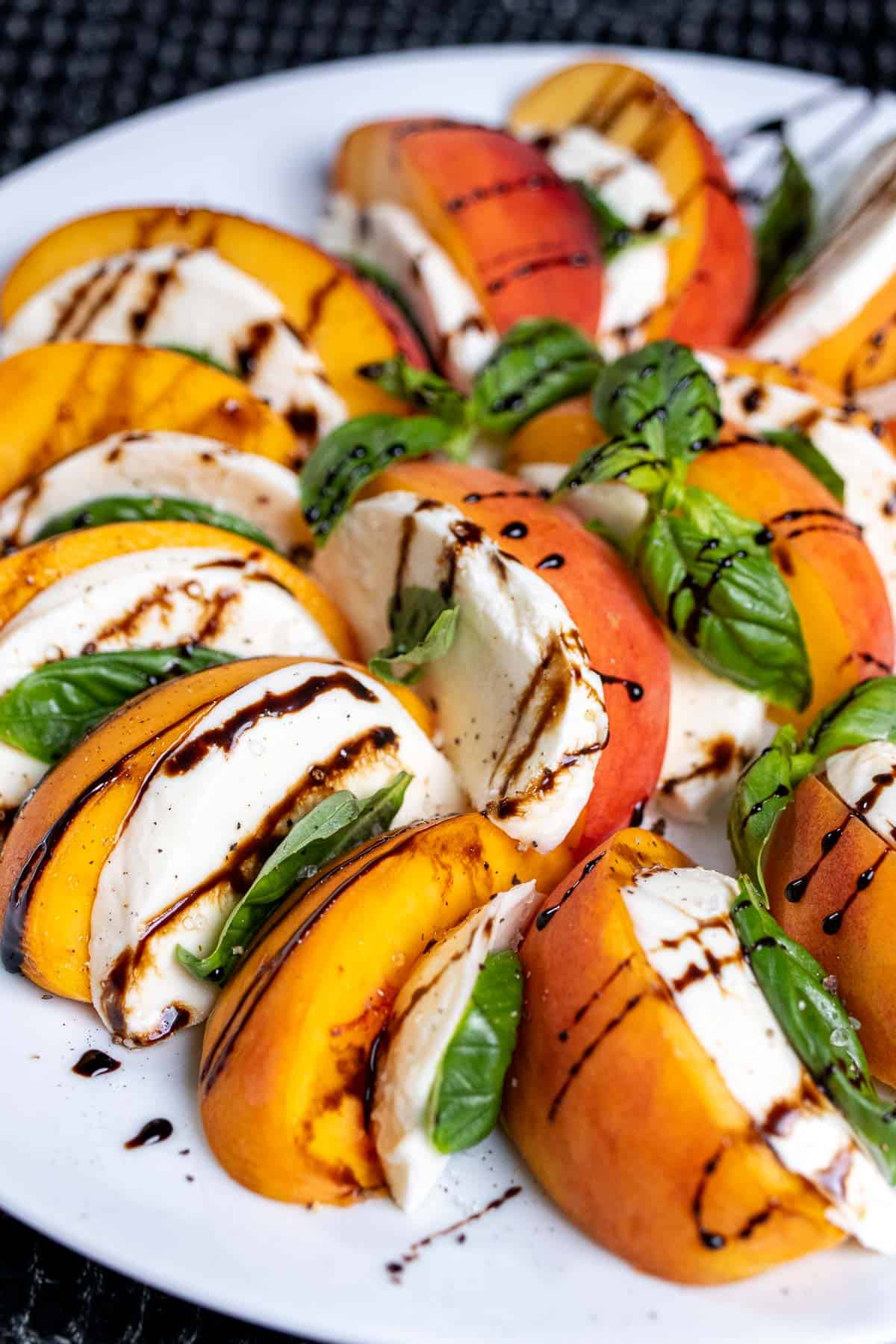 Angled view of a peach caprese salad, on a white plate with a drizzle of balsamic glaze over top.