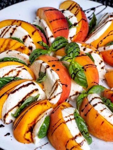 A caprese salad with peaches instead of tomatoes, on a white plate with a drizzle of balsamic glaze over top.