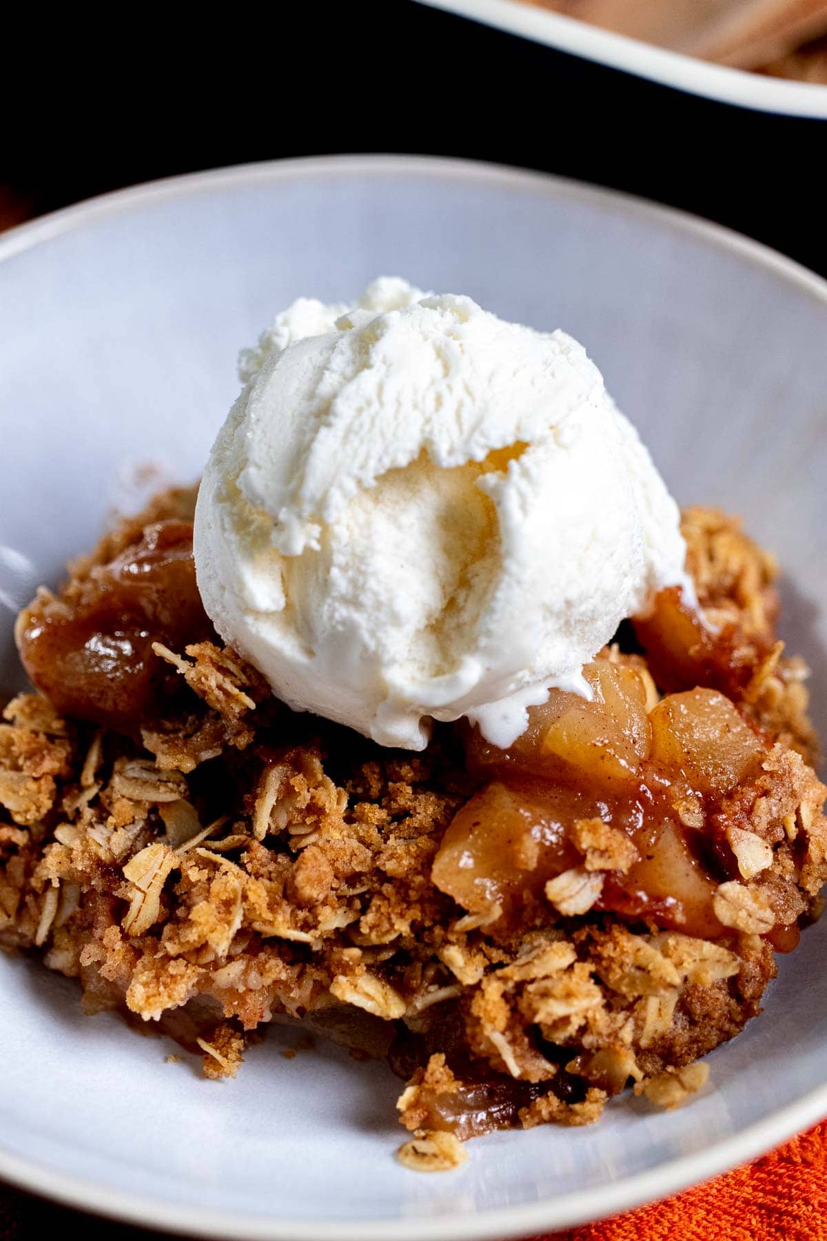 Close up of apple crisp in a white bowl, topped with vanilla ice cream.