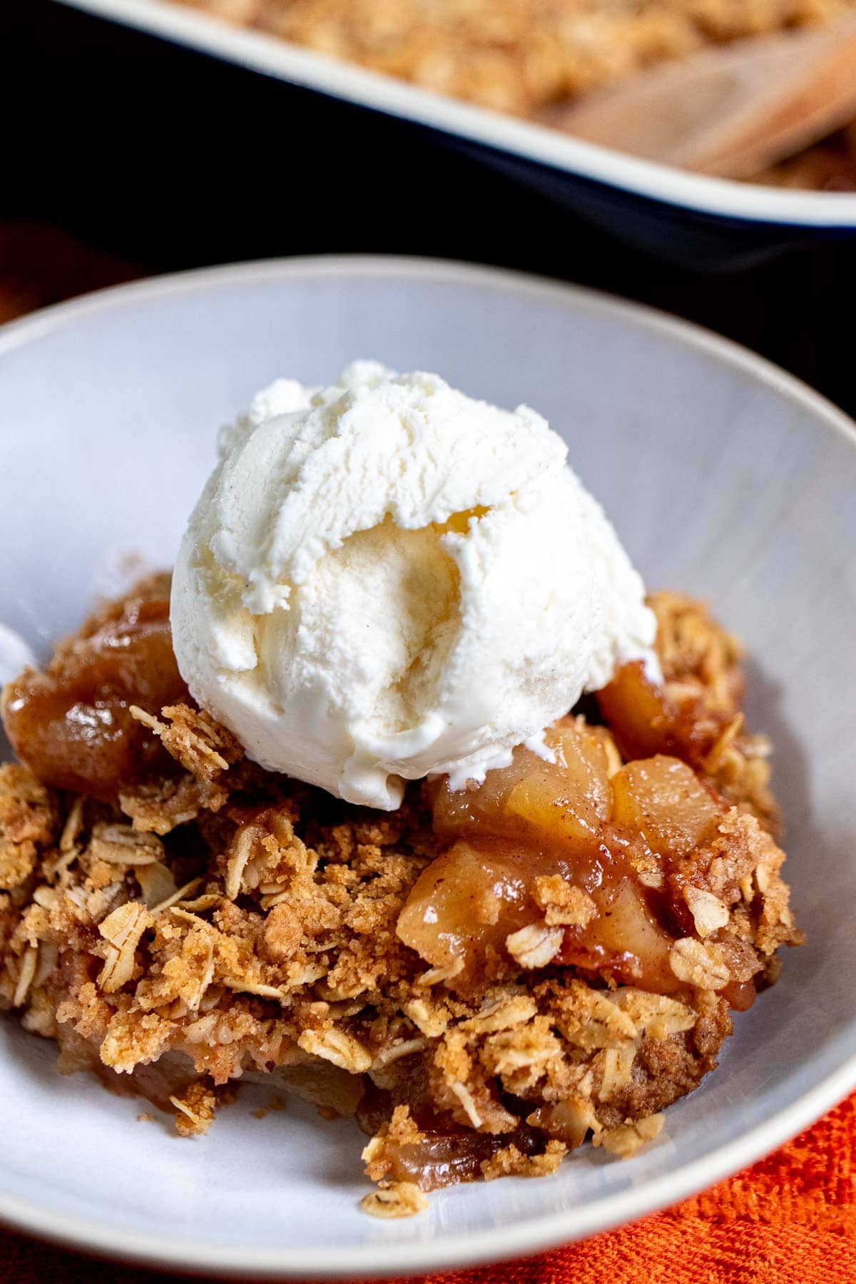 Close up of apple crisp in a white bowl, topped with vanilla ice cream.