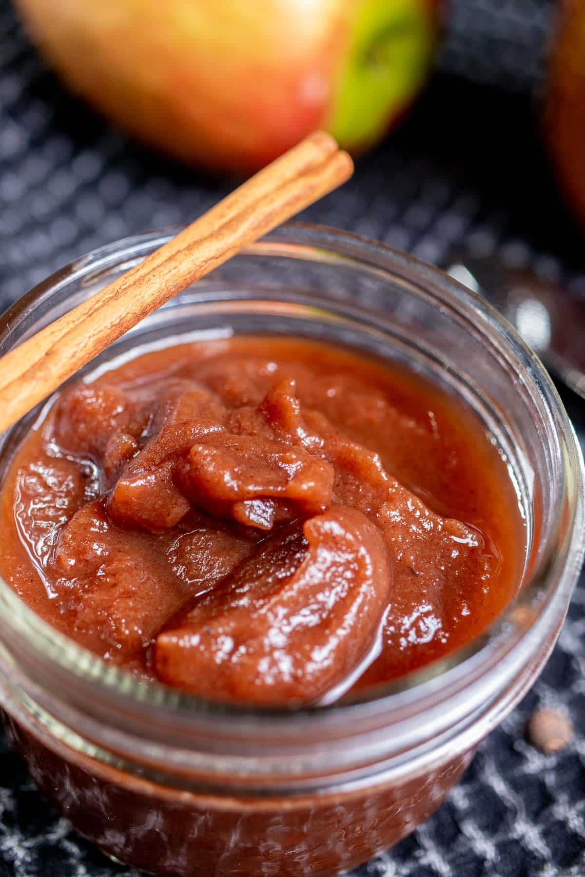 Close up of apple butter in an open, wide-mouth jar with a cinnamon stick across the top.