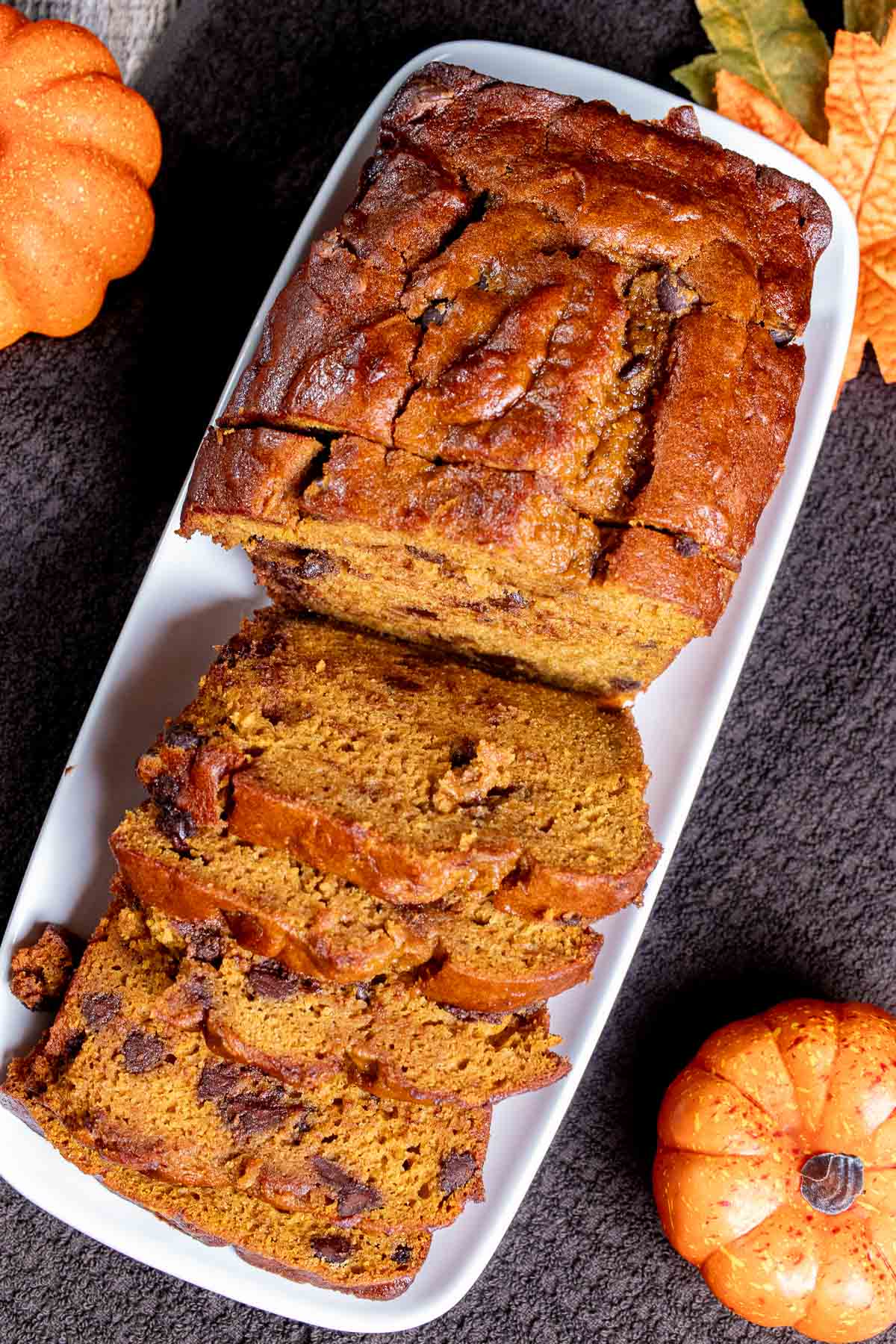Overhead view of pumpkin chocolate chip bread partially sliced on a white rectangular plate.