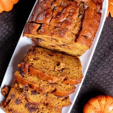 Overhead view of pumpkin chocolate chip bread partially sliced on a white rectangular plate.