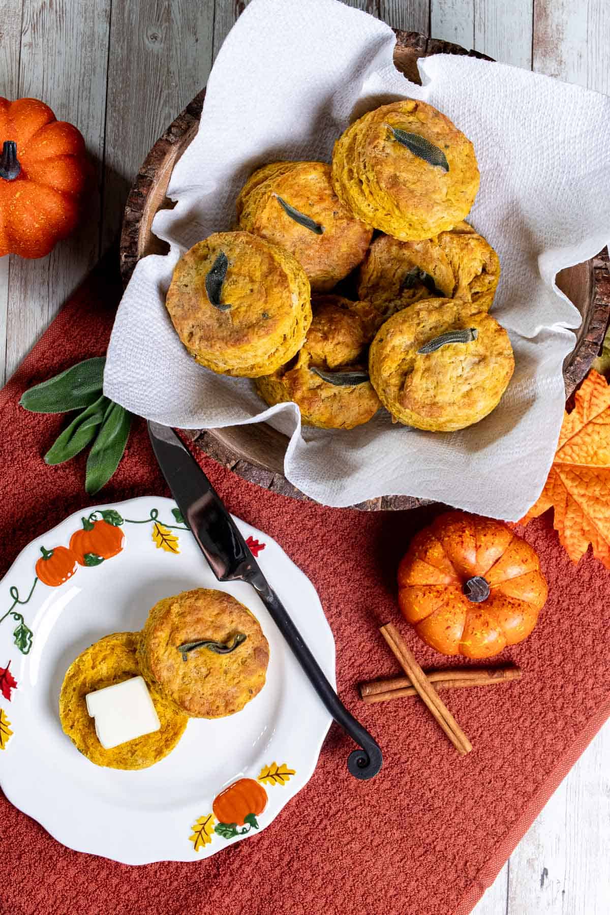 Overhead view of pumpkin sage biscuits in a basket and one cut open on a white plate.