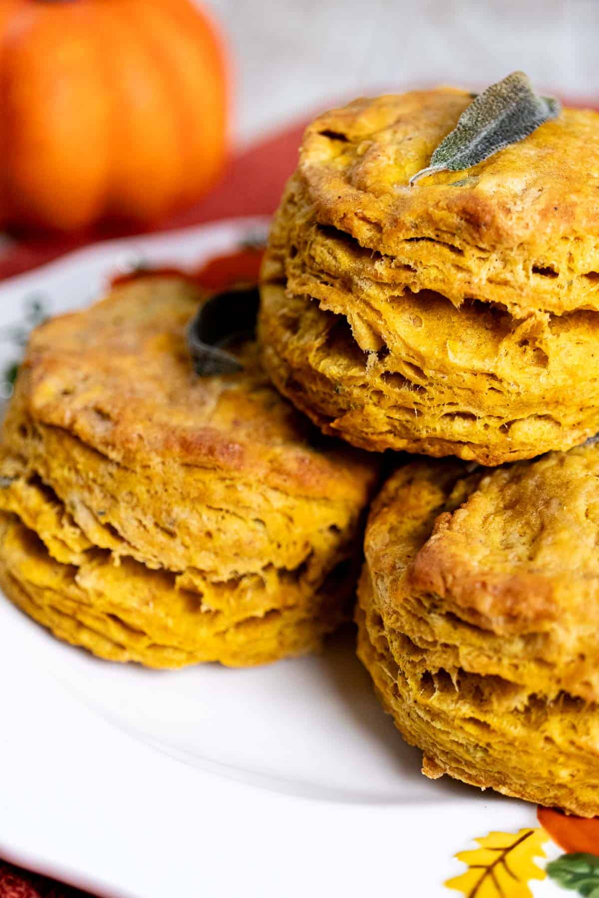 Close up view of pumpkin sage biscuits stacked on a white plate.