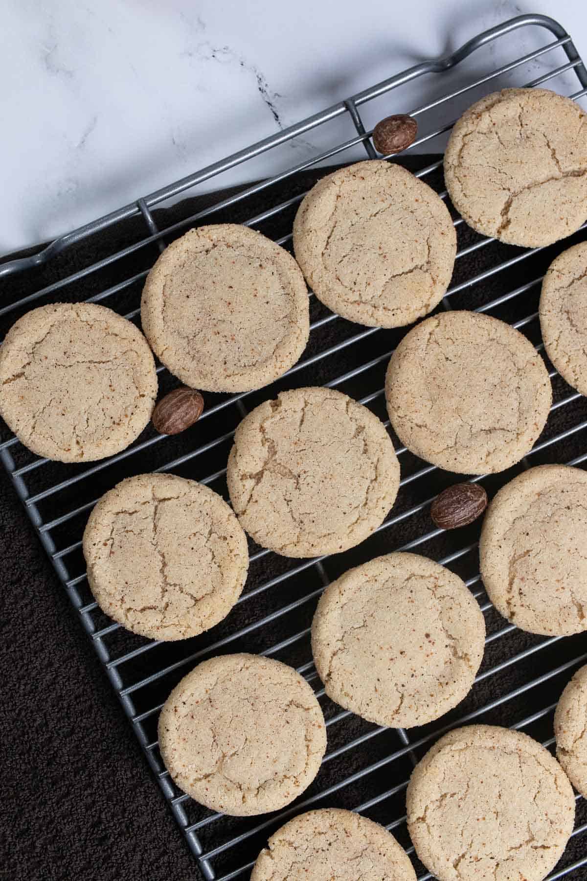 eggnog snickerdoodle cookies on a cooling rack with whole nutmegs decorating them.