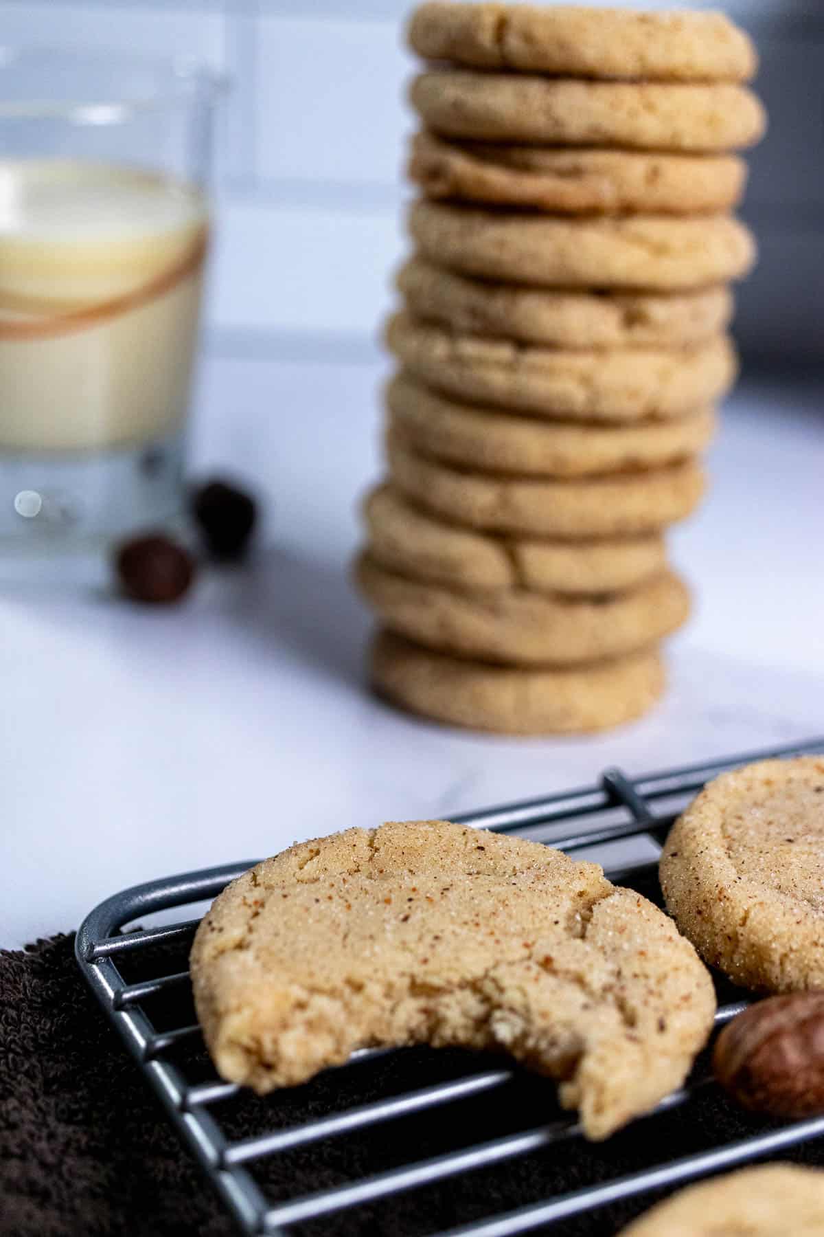 Close up of an eggnog snickerdoodle with a bite taken out of it and a stack of more cookies in the background.