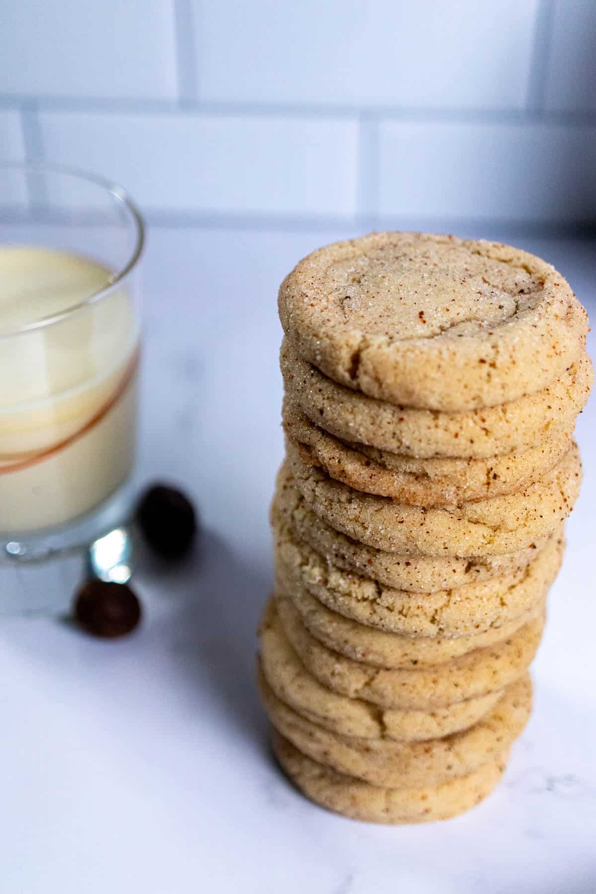 Close up view of a stack of eggnog snickerdoodles with a glass of eggnog next to them.