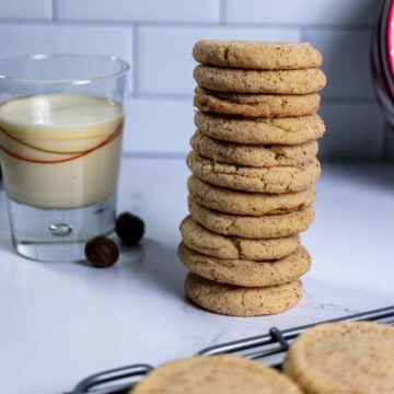 A stack of eggnog snickerdoodles on marble next to a glass of eggnog