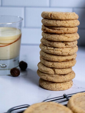 A stack of eggnog snickerdoodles on marble next to a glass of eggnog