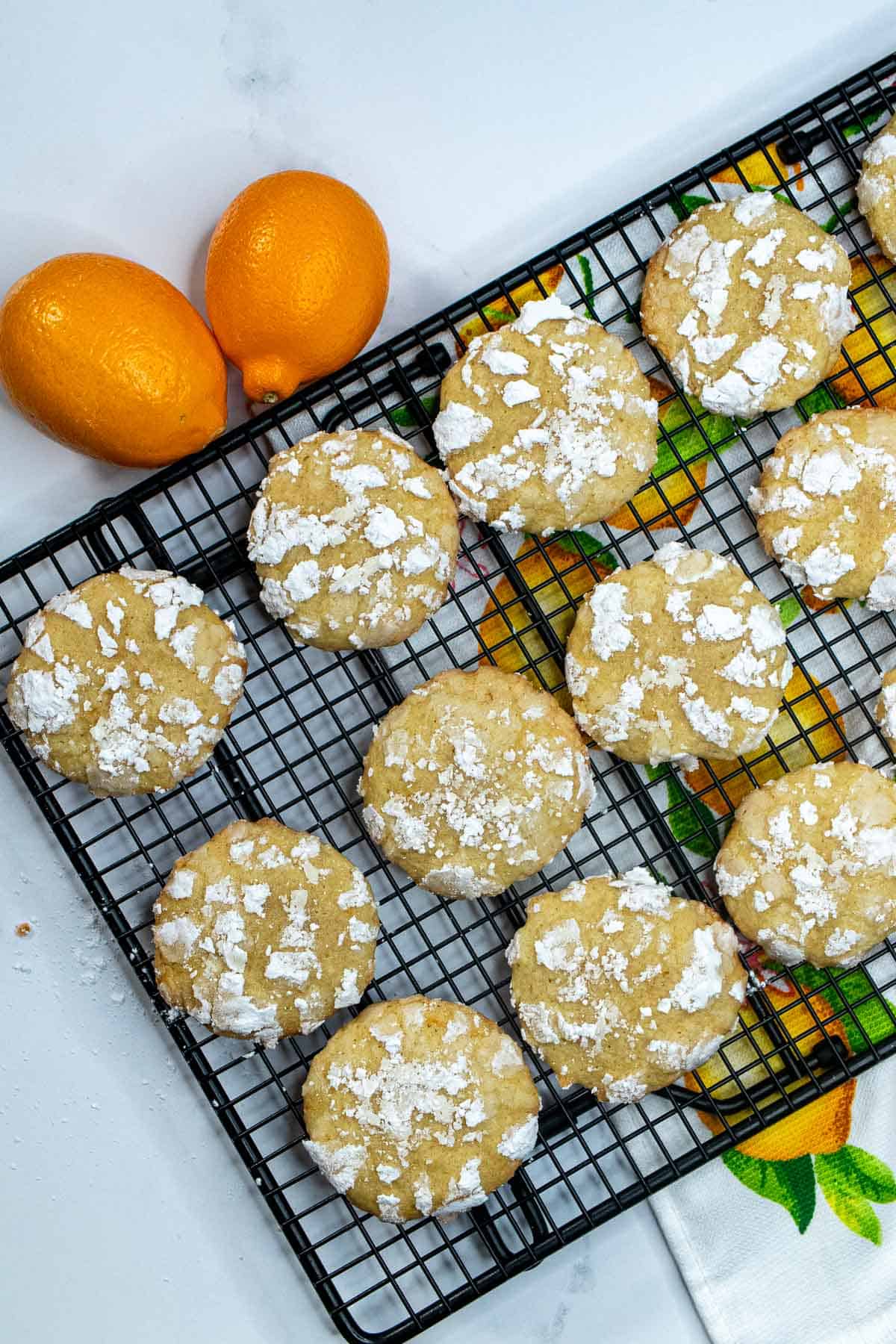 Meyer lemon cookies on a cooling rack with two Meyer lemons next to it.