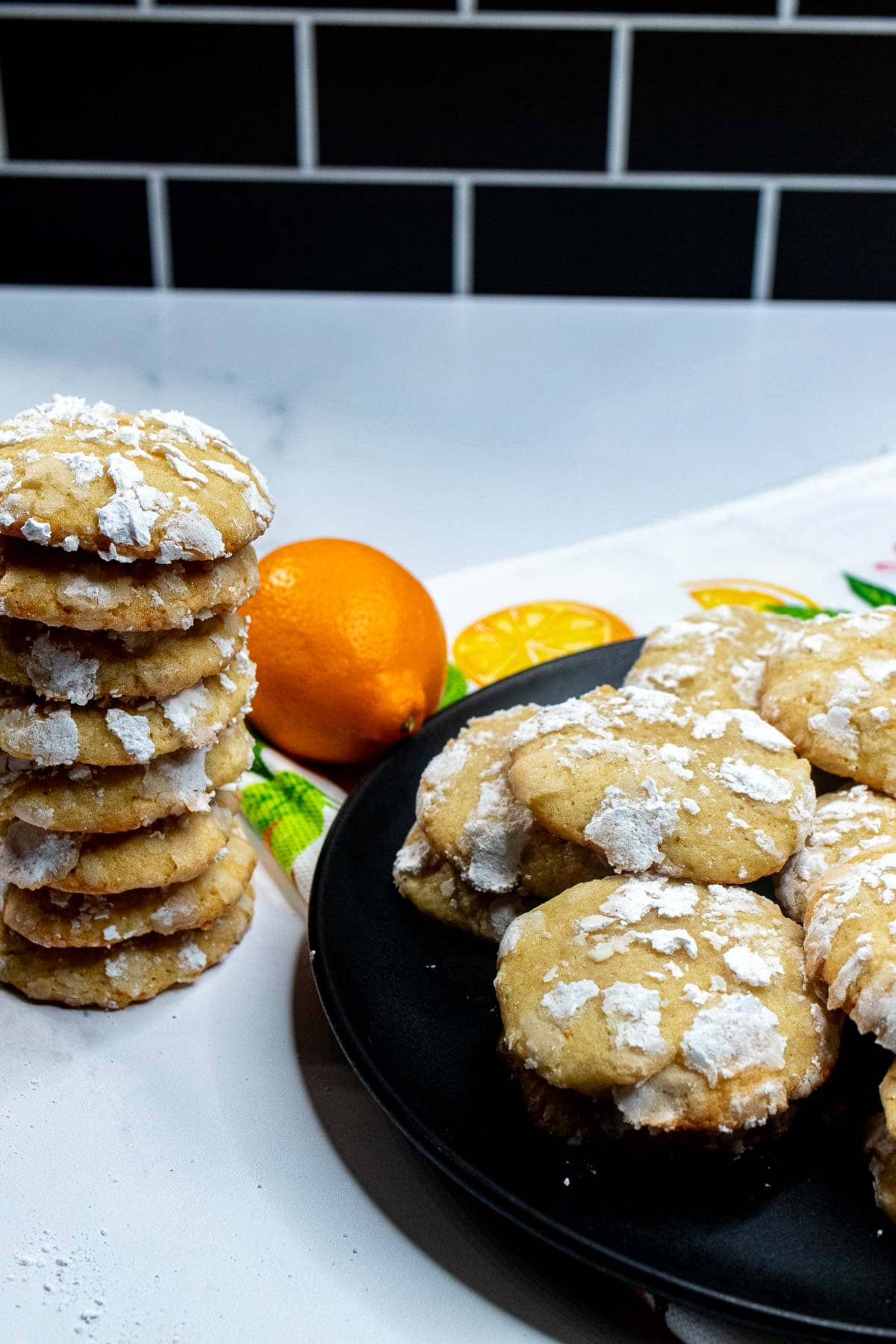A plate of lemon crinkle cookies with a stack of the cookies to the left.