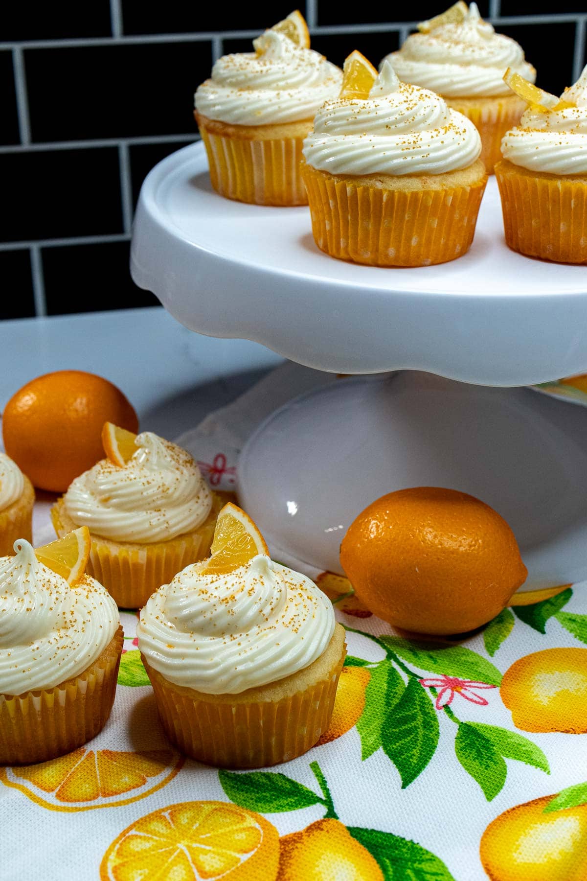 Meyer lemon cupcakes on a white cake stand with more cupcakes below it.