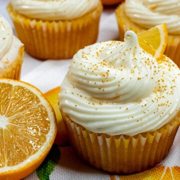 Meyer lemon cupcake with swirled cream cheese frosting next to a cut open Meyer lemon.