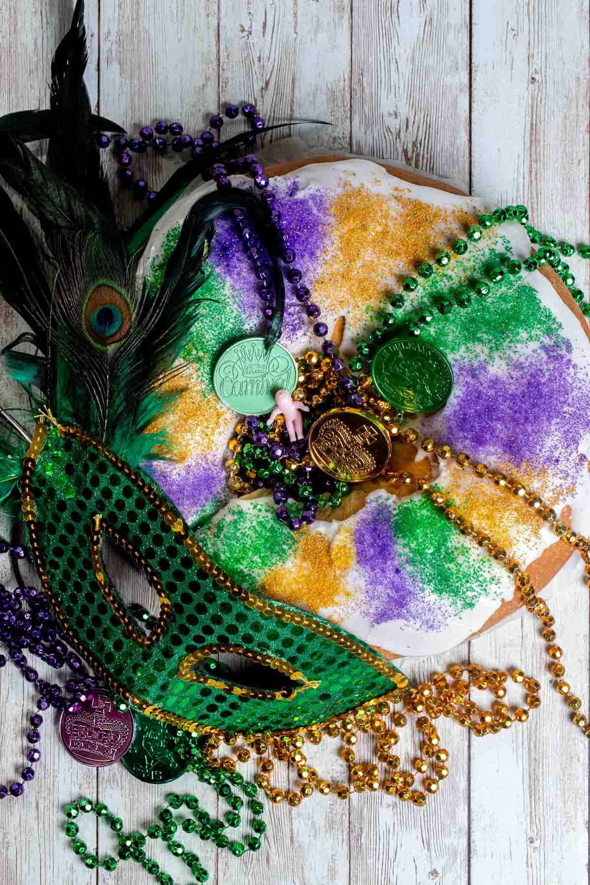 Overhead view of a traditional king cake with Mardi Gras beads and mask decorating it.