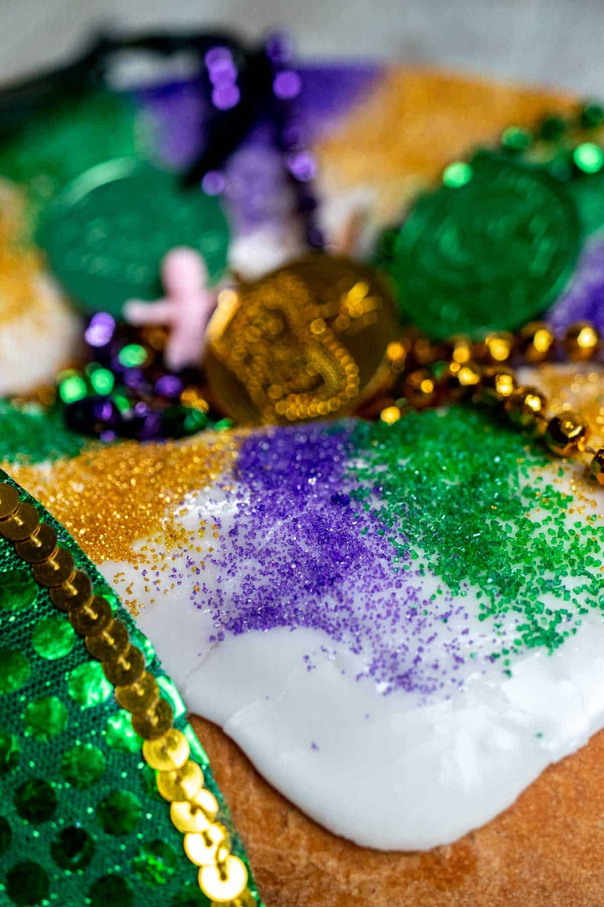Close up of the side of a king cake with icing dripping down and decorated with Mardi Gras beads