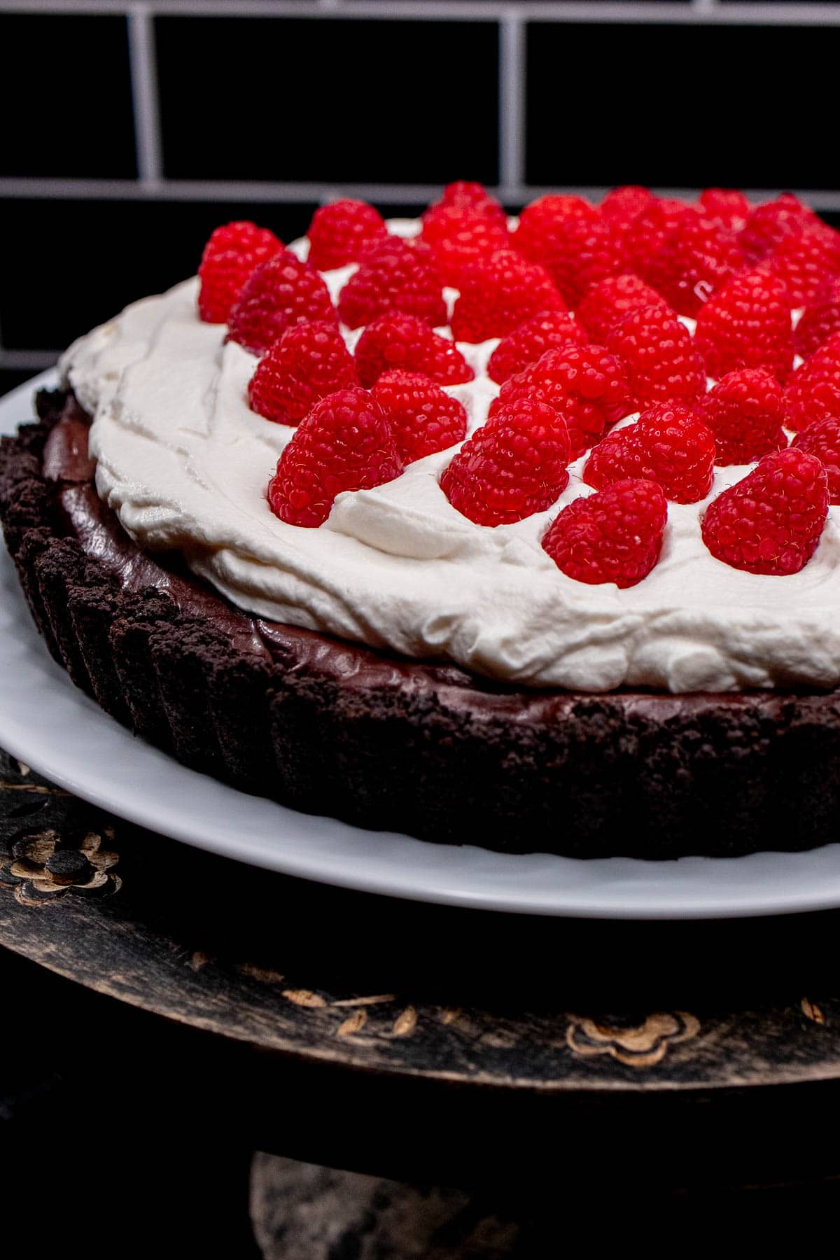A chocolate raspberry tart topped with whipped cream and fresh raspberries on a white plate.